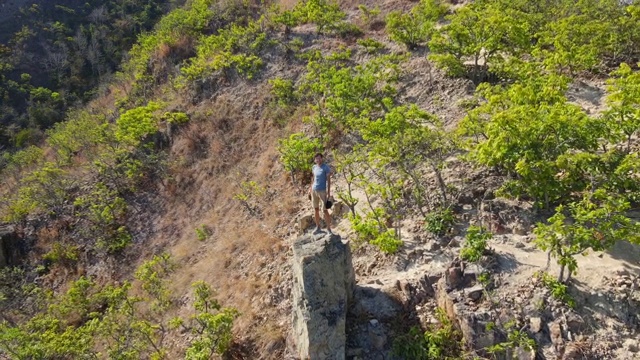 航拍的一个年轻人坐在山上的一块岩石上。徒步旅行的概念视频素材