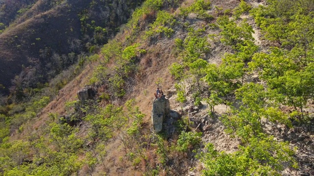 航拍的一个年轻的男人和女人坐在山上的一块岩石上。徒步旅行的概念视频素材