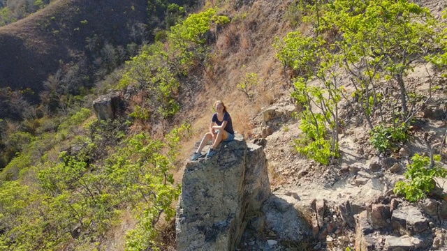 航拍一名年轻女子坐在山上的一块岩石上。徒步旅行的概念视频素材