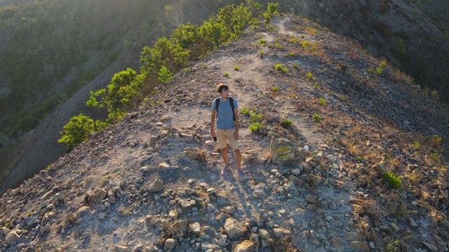 航拍的一个年轻人站在山顶上的山。徒步旅行的概念视频素材