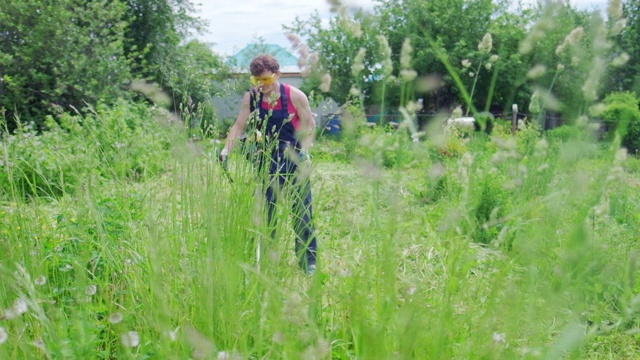 工人和割草机。一名男子用汽油修剪器修剪花园里的绿草视频素材