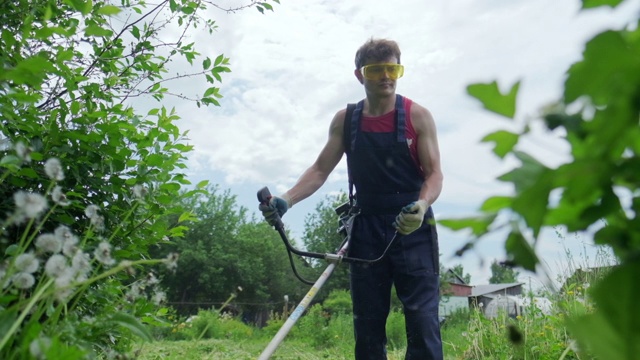 工人和割草机。一名男子用汽油修剪器修剪花园里的绿草视频素材