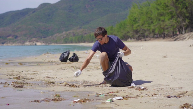 戴手套的人在海滩上收集塑料垃圾。沙滩上的垃圾问题是由人为污染造成的。环保运动，清洁环境。生态志愿服务概念视频素材