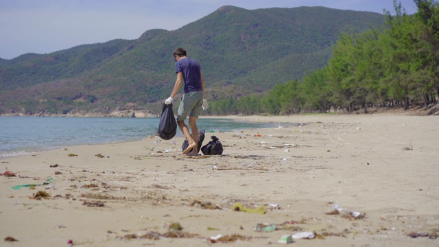 戴手套的人在海滩上收集塑料垃圾。沙滩上的垃圾问题是由人为污染造成的。环保运动，清洁环境。生态志愿服务概念视频素材