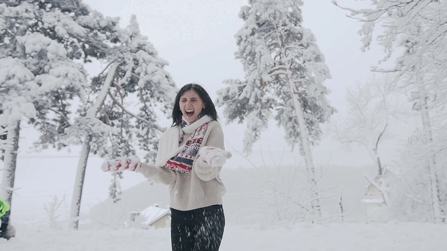 黑发女人在度假抛雪在空中森林与一个美好的微笑。可爱的女孩戴着红白相间的围巾和针织手套，还有时髦的毛衣。好天气和下雪视频素材