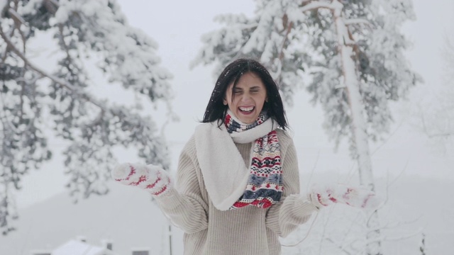 黑发女人在度假抛雪在空中森林与一个美好的微笑。可爱的女孩戴着红白相间的围巾和针织手套，还有时髦的毛衣。好天气和下雪视频素材