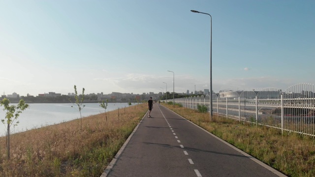 男子骑着长板在江边的空笔直的道路上的面部鸟瞰图。暑假潮人骑滑板在城市外的日落时间4k视频素材