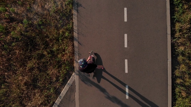 鸟瞰图男子骑长板在空的直线道路。暑假，那个家伙在日落时分玩滑板。摄像机拍了4k视频素材