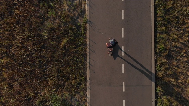 鸟瞰图男子骑着长板在空笔直的道路在日落时间。镜头跟随潮人在暑假骑滑板4k视频素材