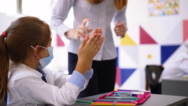 年轻女教师在教室里消毒她的学生的手视频素材