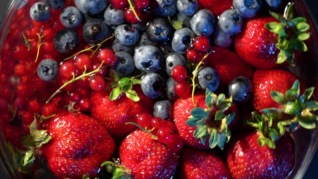 4 k。各种五颜六色的浆果在玻璃上吹旋转在黑色的背景上，草莓，覆盆子，黑莓，蓝莓，健康的食品概念。视频素材