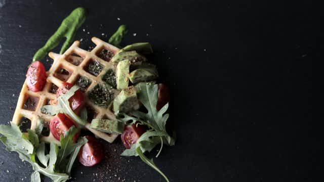 使食物俯视图。新鲜出炉的比利时华夫饼配芝麻菜、番茄和牛油果放在黑色盘子里。美味的华夫饼。早餐的概念视频素材