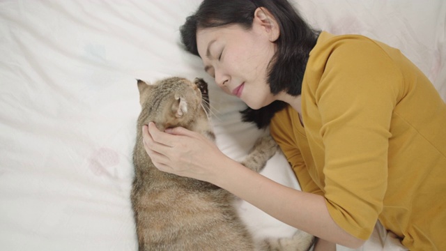 亚洲女人和虎斑猫一起躺在床上。视频素材