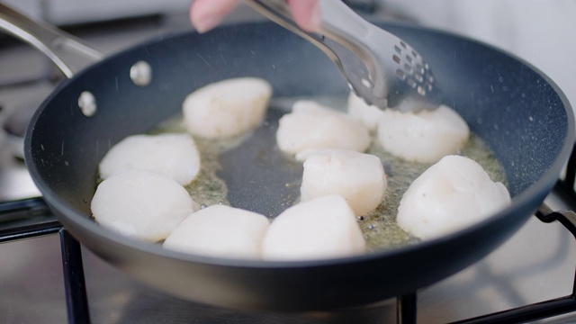 在煤气炉上的平底锅里用油煎多个扇贝的特写。用慢镜头烹饪炸扇贝的概念。视频素材