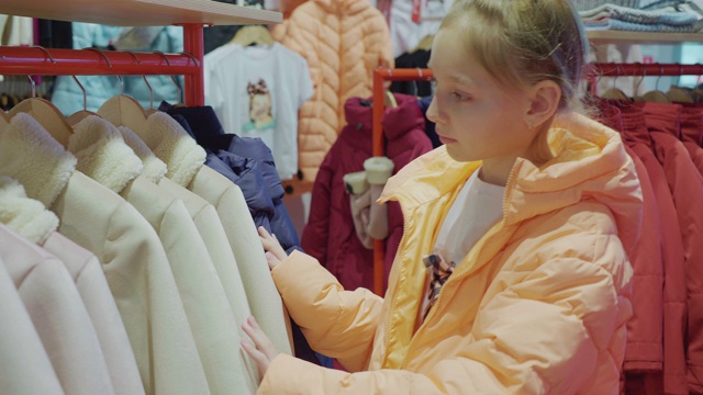 少女在时装陈列室挑选夹克。年轻女子在商店里看衣服。少女在服装店购物。视频素材