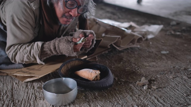 一个行走的人给钱的老人无家可归的人躺在地板上被遗弃的建筑，他醒来，高兴地得到钱视频素材