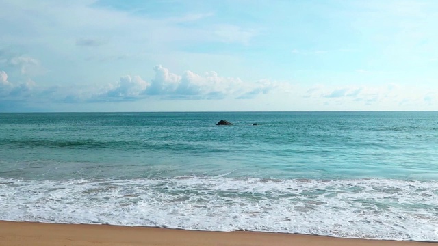 美丽的深蓝色的海水和白色的平静的海浪撞击沙滩晴朗的蓝天背景视频素材