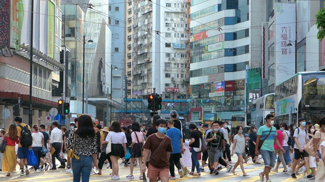 高峰时段，一群带着防护口罩的繁忙通勤者穿过市中心街道，背景是高楼大厦和繁忙的交通视频下载