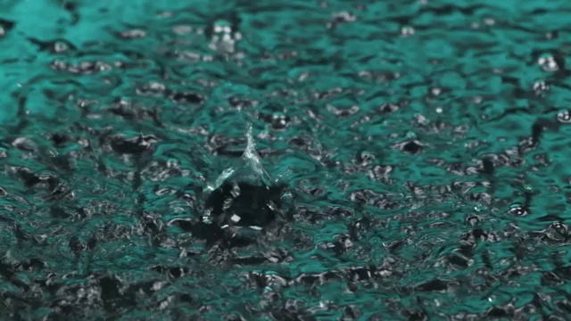 雨滴落在绿色的水中。特写水滴，飞溅，水面上的涟漪。视频素材