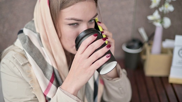 年轻女子在咖啡馆喝着咖啡，在街上打电话视频素材