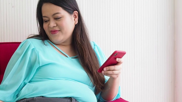 大码亚洲女性喜欢吃甜甜圈和在家里使用智能手机视频素材