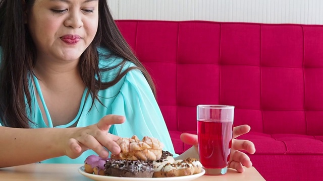 近手加大尺寸的女人喜欢坐在房间的红色沙发上吃甜甜圈视频素材