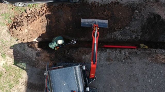 小型挖掘机和工人埋设在城市街道上的沟渠用管道、架空视频素材