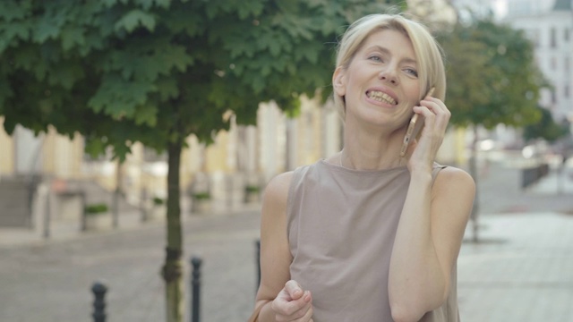 特写的自信的中年白人妇女走在城市的街道上和讲电话。肖像快乐优雅的金发女士享受阳光明媚的夏日户外。视频素材