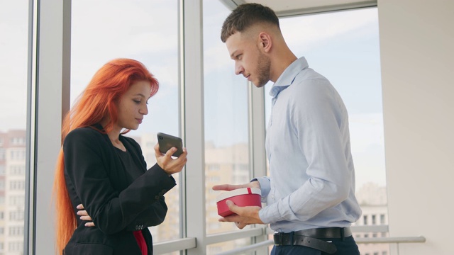 男人给红头发的女人礼物。一个打电话的女人从她的丈夫那里收到了一份礼物，并且在办公室里很高兴收到这份礼物。视频素材