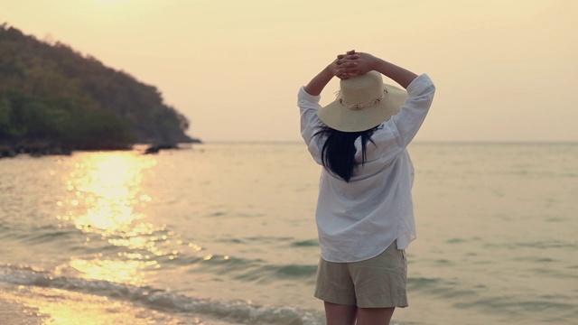 年轻的亚洲女人旅行者伸展双臂举起感觉放松享受一个假期的夏天，而站在海滩上。视频素材