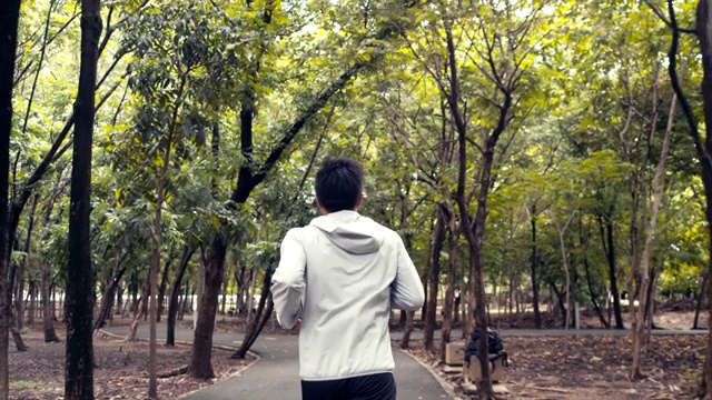 年轻的亚洲男子运动员在一个公园里跑步，享受美丽的森林。视频素材