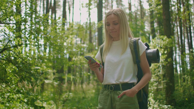 迷人的女人在森林里放松，在户外使用智能手机。在森林里徒步旅行的女人在智能手机上打字。独自使用智能手机的女性徒步旅行者。视频素材