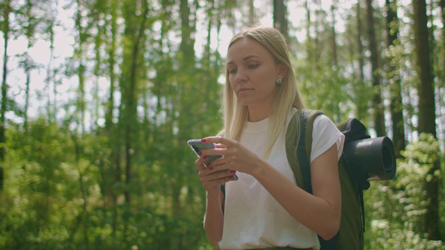 迷人的女人在森林里放松，在户外使用智能手机。在森林里徒步旅行的女人在智能手机上打字。独自使用智能手机的女性徒步旅行者。视频素材