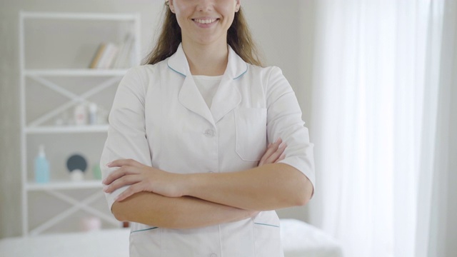 陌生的年轻女医生交叉着双手微笑着。自信的黑发白种女人在医院病房的工作场所摆姿势。专业医师在室内。视频素材