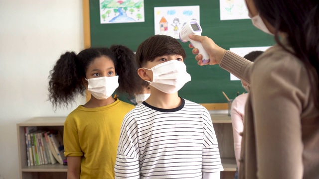 一组学生在教学楼内进行温度检查和扫描。小学生们都戴着口罩，排队进入教室。视频素材