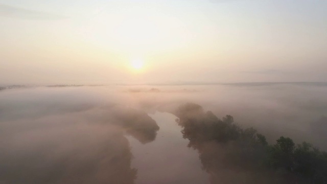 航拍美丽的薄雾景观日出在清晨。令人惊叹的风景山谷与河流覆盖在浓雾。黎明时分，在美丽的乡村环境中飞翔。慢动作视频素材