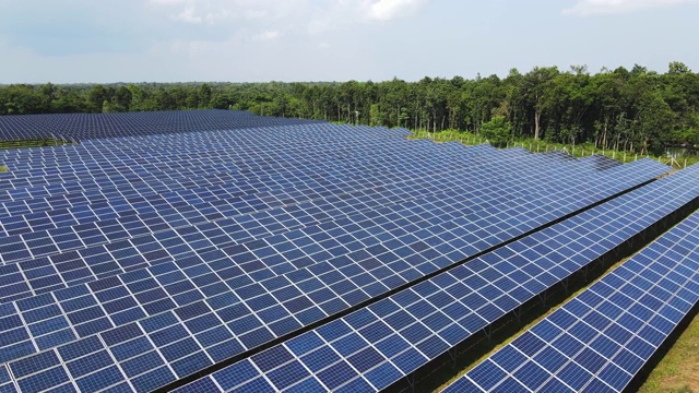 太阳能电池板或太阳能电池在太阳能农场的俯视图与绿树和阳光反射在蓝天背景，概念太阳能光伏电站领域。视频下载