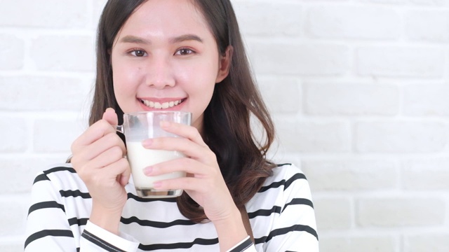 迷人的亚洲女人喝牛奶和微笑在家里近距离面对。健康的生活方式。视频素材