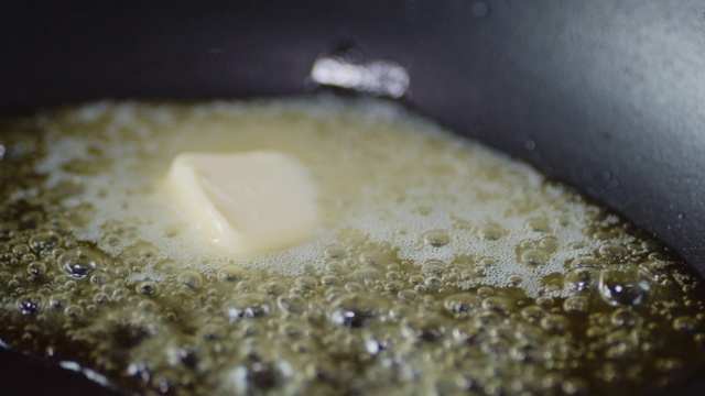 一块油在平底锅中融化，伴随着热气和气泡。视频素材