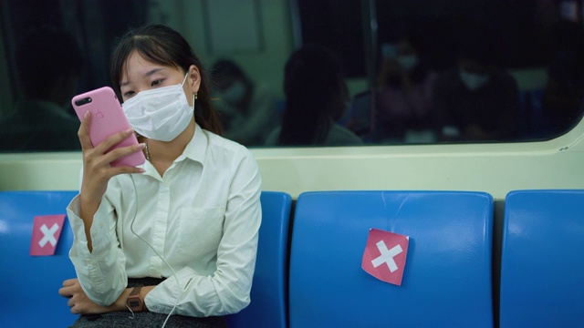 一名年轻的亚洲女子戴着医用口罩在地铁上使用智能手机视频素材