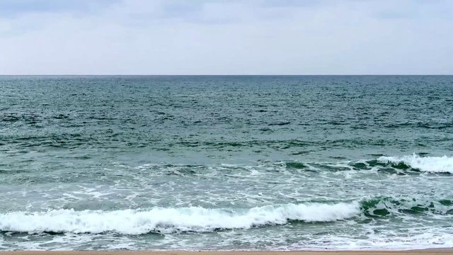 深蓝绿色平静的海浪在多云的天空背景下撞击热带沙滩的特写视频素材