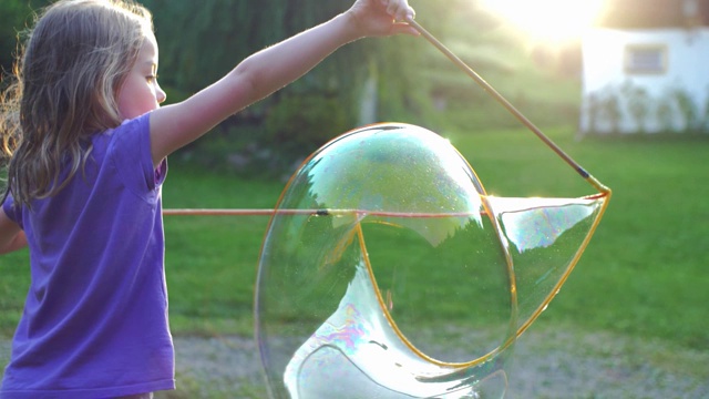 小女孩玩巨大的肥皂泡在日落背光的观点视频素材