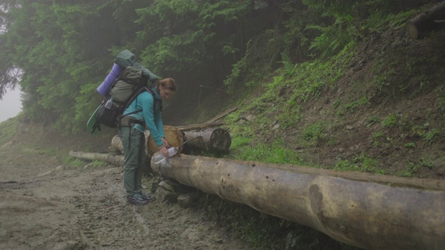 女徒步旅行者背包装满瓶子与清澈的山涧水。喝着清澈的山水的女人。迷雾森林中的游客。视频素材