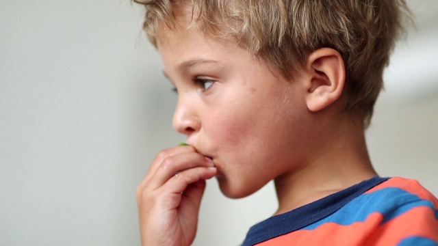 孩子吃水果零食。沉思中的蹒跚学步的男孩咬了一口健康的草莓视频素材