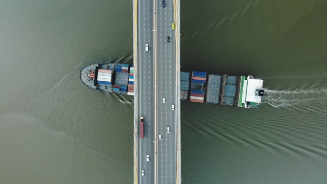 鸟瞰图/一艘大型货船在河上的一座桥下行驶，桥下车辆川流不息。视频素材
