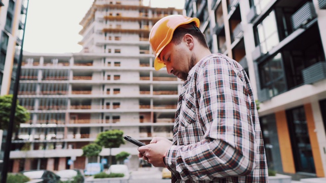 年轻工程师在建筑工地使用智能手机。建筑师使用电话。经理开发建设智能手机短信。在检查和验证过程中，建设者在应用中做了记录视频素材