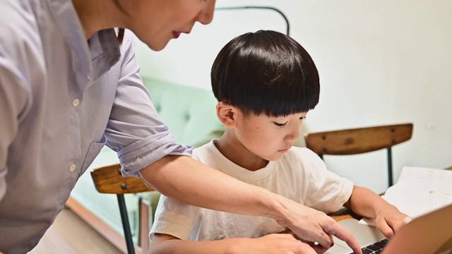 一个用笔记本电脑在家学习的儿子。他的母亲教学习。视频素材