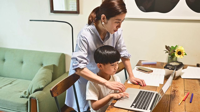 一个用笔记本电脑在家学习的儿子。他的母亲教学习。视频素材