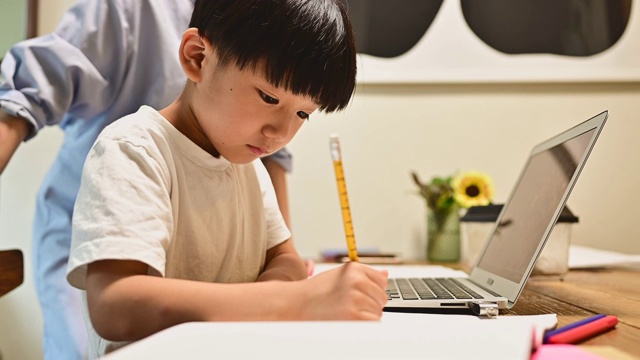 一个用笔记本电脑在家学习的儿子。他的母亲教学习。视频素材