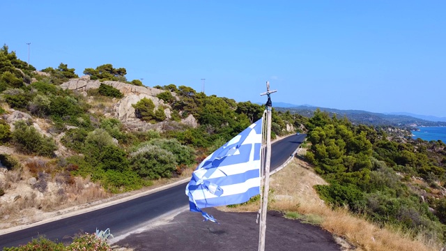 希腊国旗迎风飘扬，旅游道路上有过往车辆，国旗后面是蓝色的大海视频素材